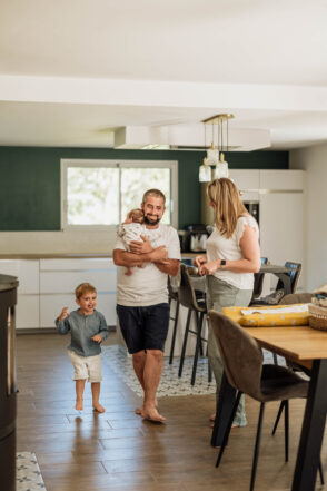 Une famille souriante dans sa cuisine, partageant un moment de complicité lors d'une séance photo naissance lifestyle au nord de Rennes en Ille-et-Vilaine
