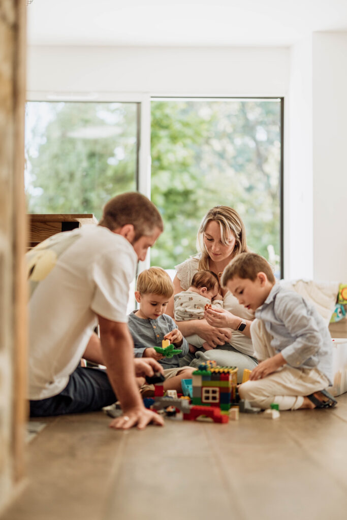 Une famille jouant tous ensemble avec leurs enfants dans leur maison, partageant un moment de complicité lors d'une séance photo naissance au nord de Rennes en Ille-et-Vilaine